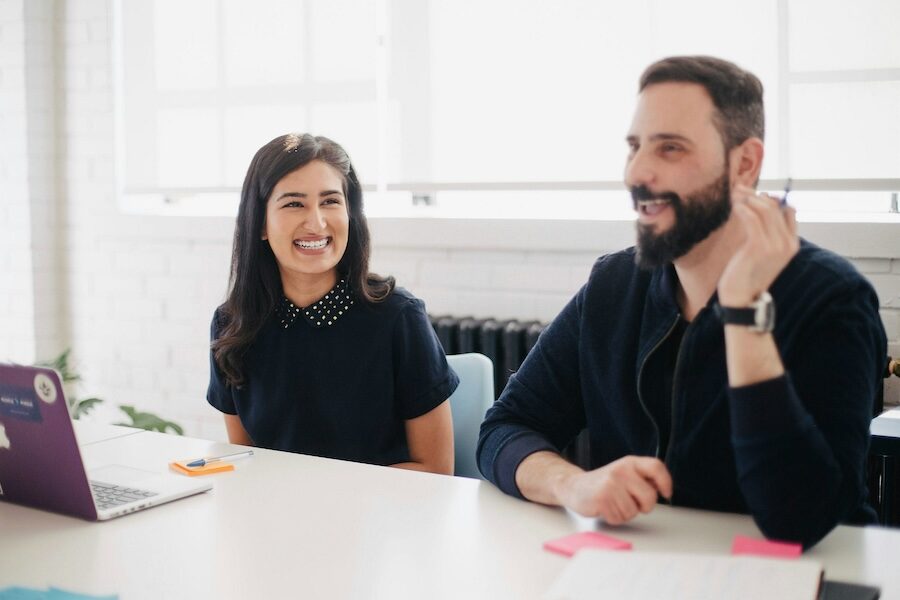 two people team laptop smiling laughing happy pen office