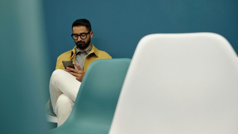 man glasses on phone waiting in waiting room chair