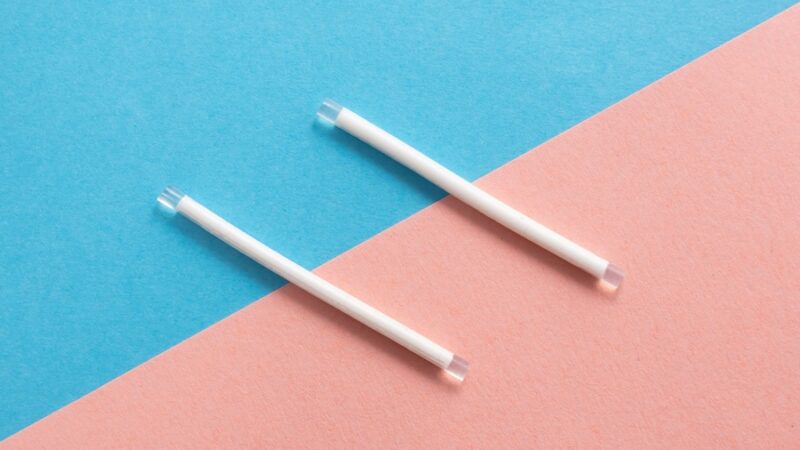Two contraceptive implant rods on a blue and pink background