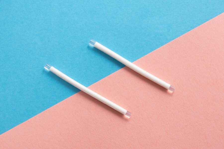 Two contraceptive implant rods on a blue and pink background