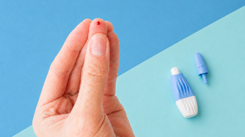 Finger with a drop of blood beside an opened finger-prick lancet