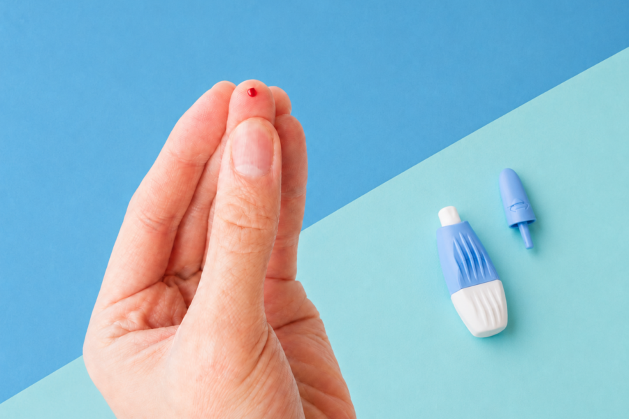 Finger with a drop of blood beside an opened finger-prick lancet